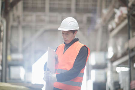 Young male warehouse worker examining plank in warehouseの写真素材