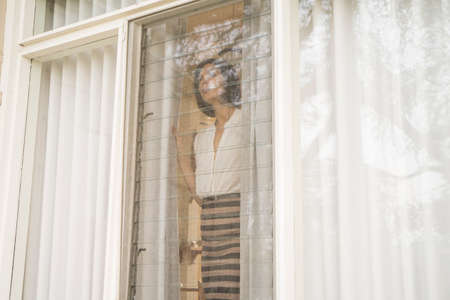 Mid adult woman looking out of house windowの写真素材