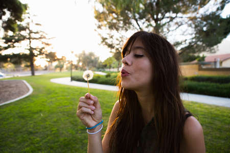 Young woman blowing dandelion clock in park
