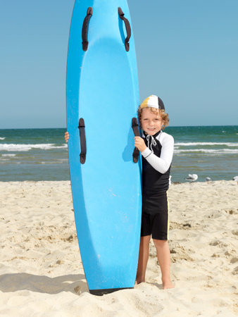 Portrait of cute boy nipper (child surf life savers) next to surfboard at beach, Altona, Melbourne, Australiaの写真素材