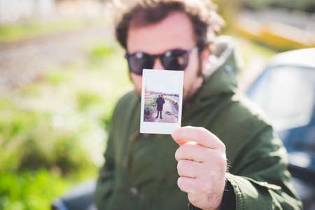 Portrait of mid adult man holding up an instant photograph of himself