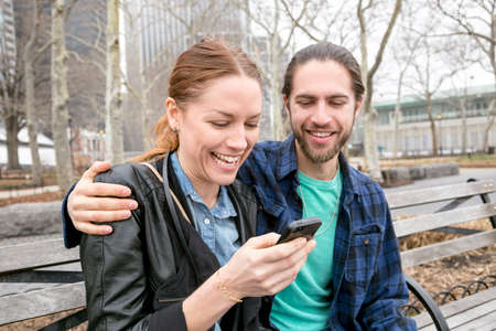 Couple checking messages on park bench, New York, New York, USAの写真素材