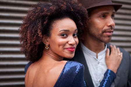Couple standing outdoors, hugging, looking at camera, smiling