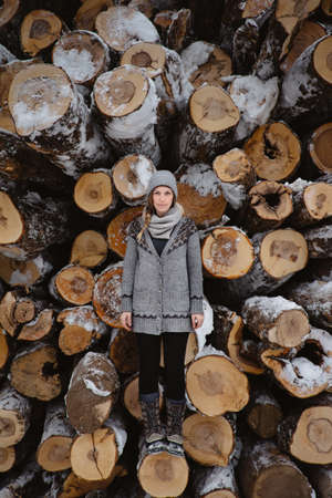 Woman standing against stack of logs in winter