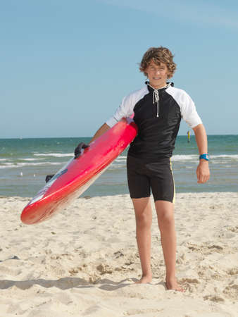 Portrait of teenage boy nipper (child surf life savers) carrying surfboard, Altona, Melbourne, Australiaの写真素材