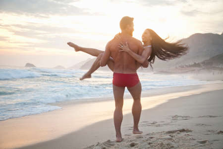 Mid adult couple on beach,man carrying woman in arms, rear viewの写真素材