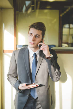 Portrait of young businessman commuter using digital tablet and smartphone on train.の写真素材