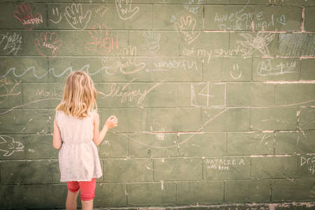 Girl in front of wall with chalk drawings, rear viewの写真素材