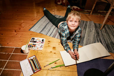 Boy lying on floor with watercolor paints and sketch padの写真素材