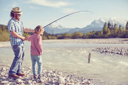 Mid adult man and boy near river holding fishing rod with fish attached, Wallgau, Bavaria, Germanyの写真素材