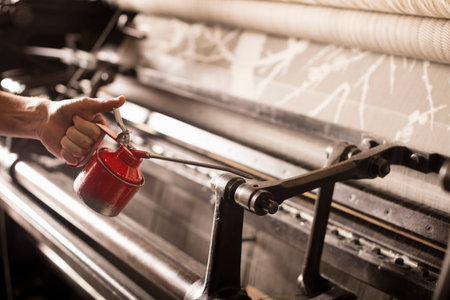 Hand of male weaver oiling old weaving machine in textile mill