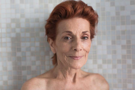 Bare shoulder portrait of smiling mature woman with short red hair