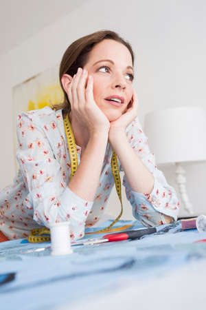 Mature woman with tape measure resting on elbows, chin on hands looking away