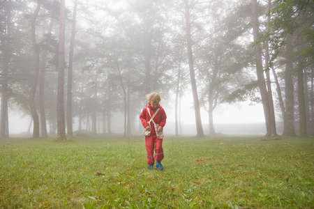 Boy wearing red waterproofs searching in misty landscapeの写真素材