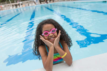 Portrait of girl in swimming pool wearing swimming goggles, looking at camera smilingの写真素材
