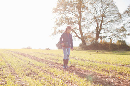 Girl wearing headphones using metal detector in sunlit fieldの写真素材