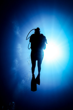 Silhouetted man scuba diving in ocean, Bali, Indonesiaの写真素材