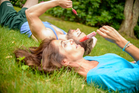 Mature woman and young man lying on grass, eating ice lolliesの写真素材