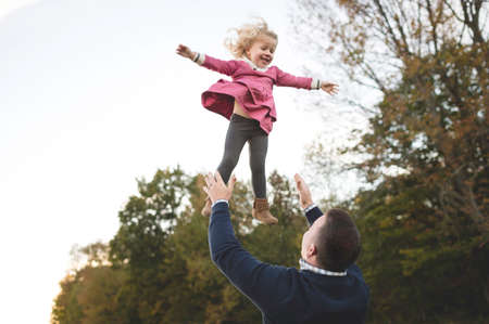 Mid adult man throwing young daughter mid air