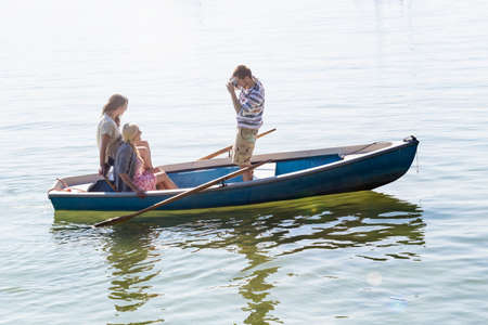 Side view of young man in boat on lake photographing womenの写真素材