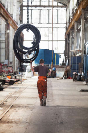 Rear view of worker pulling piping on winch in shipyard workshop
