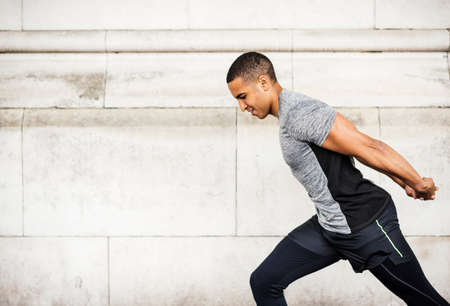 Side view of young male runner warming up with hands behind back