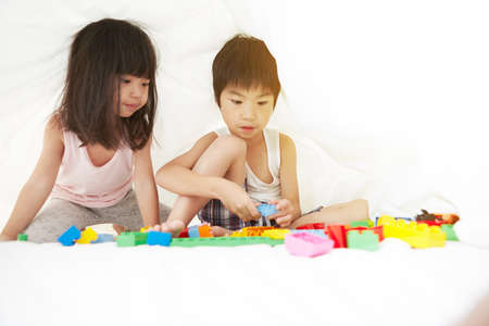 Young Chinese boy and girl in bed playing with their toys under the bedsheets