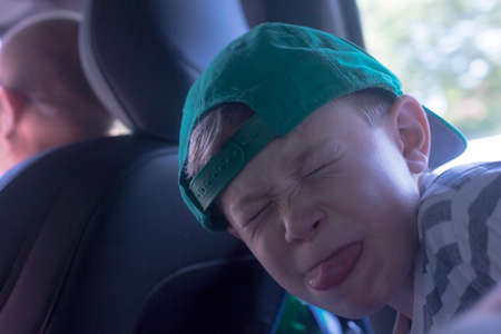 Portrait of boy wearing baseball cap pulling face in car