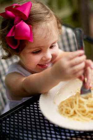 High angle view of girl with pink hair bow sitting at garden eating spaghettiの写真素材