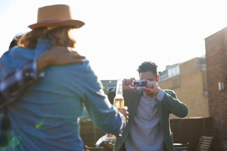 Young man photographing male friends at rooftop party