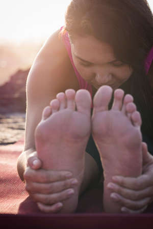 Close up of woman holding her feet practicing yoga at dawnの写真素材