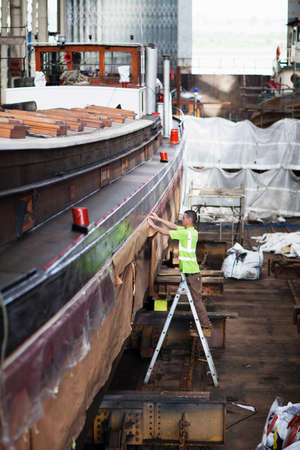 Worker on step ladder checking boat in shipyard workshopの写真素材