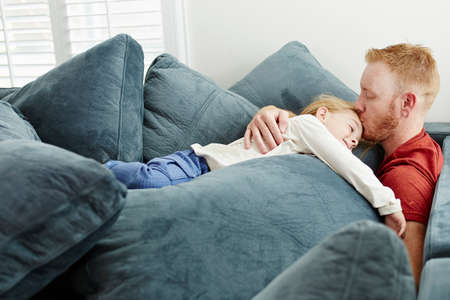 Father and daughter lying on pile of cushions in living roomの写真素材