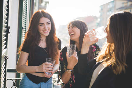Three young female friends laughing and chatting on waterfront balconyの写真素材