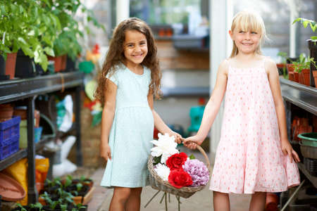Portrait of two girls holding basket of fresh flowers in greenhouseの写真素材