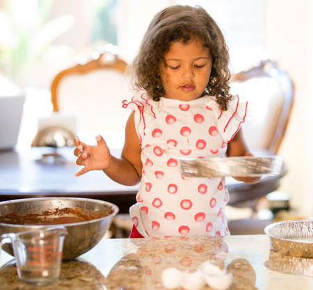 Girl at kitchen counter holding cake tin looking downの写真素材