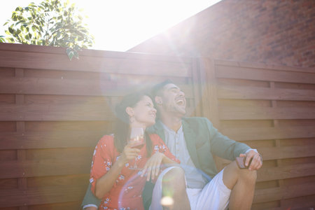 Relaxed mid adult couple laughing and drinking at rooftop partyの写真素材