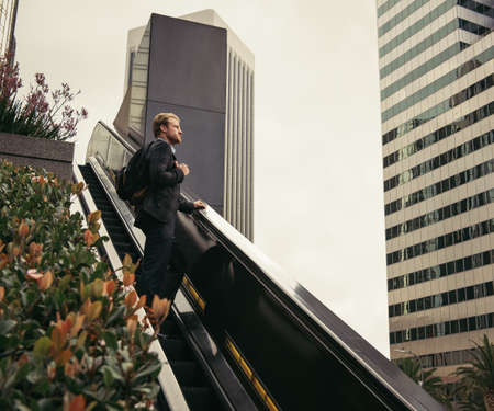 Businessman moving up escalator, Los Angeles, USAの写真素材