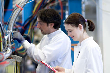 side view of male and female colleagues wearing lab coats, holding clipboard