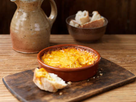 Bowl of smoked cheese bake, crusty bread on wooden chopping board