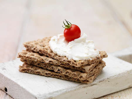 Soft cheese and cherry tomato on stack of crackers