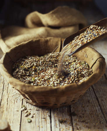 Organic bakery ingredients, mix of pumpkin, sunflower, poppy and flax seeds pouring into wicker bowlの写真素材