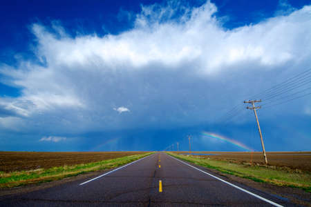 A highway leads to a storm and a rainbow west of Healy, Kansas, USAの写真素材