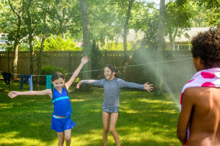 Three children playing garden with garden hoseの写真素材