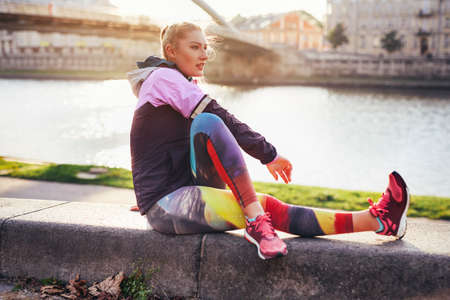Mid adult female runner doing warm up exercise on riverside wallの写真素材