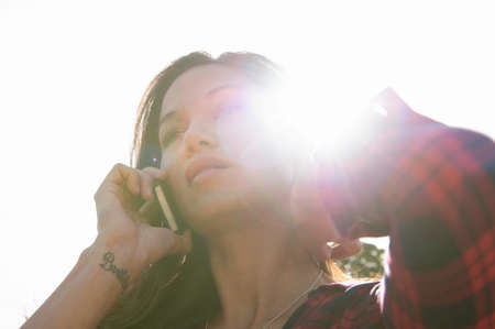 Young woman talking on smartphone against sunlit skyの写真素材