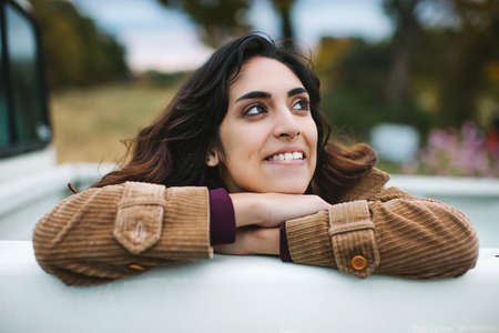 Young woman in back of truck, leaning on edge of truck, smiling, looking awayの写真素材