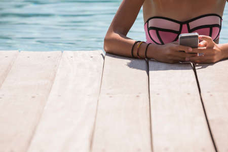 Cropped shot of girl in swimming pool using smartphone
