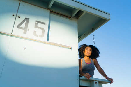 Mid adult woman standing on look out tower at beach, looking at viewの写真素材