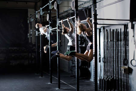 Three young adults training on wall bar in crossfit gymの写真素材